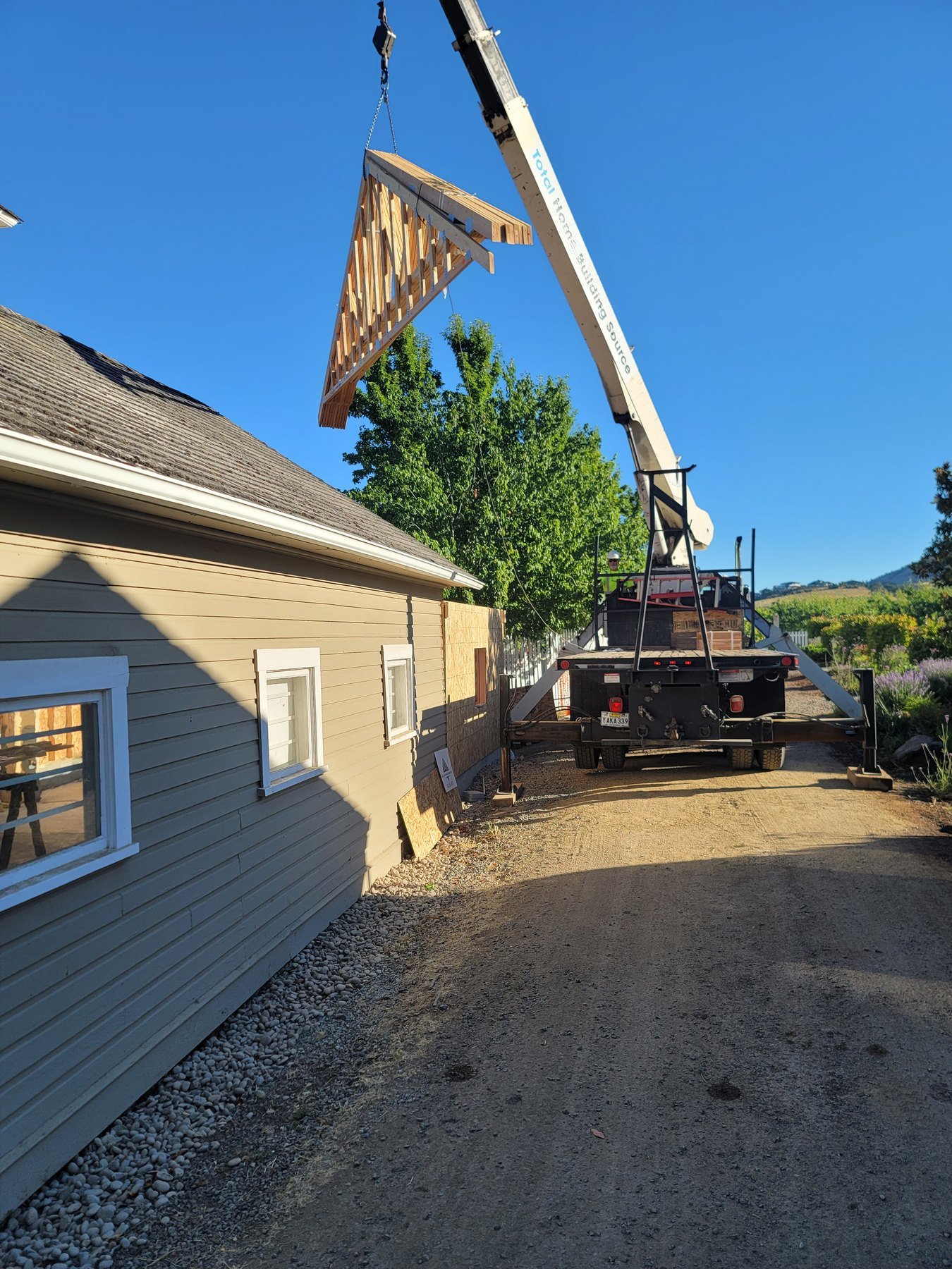 Crane lifting a roof truss beside a house