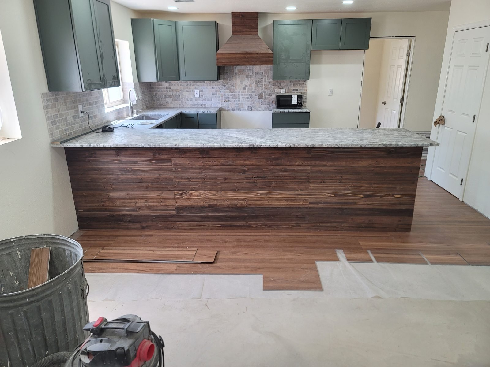 Green kitchen cabinets and wood peninsula with flooring in progress