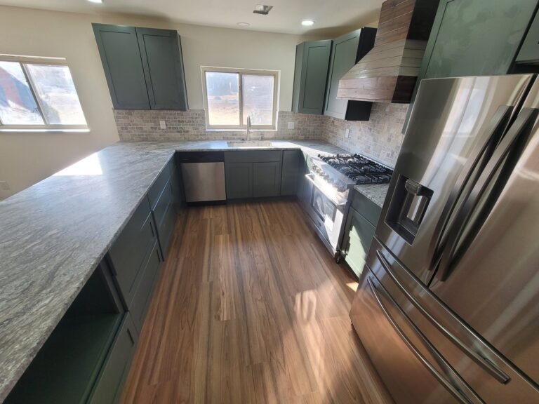 Kitchen sink area with green cabinets and wood-look flooring