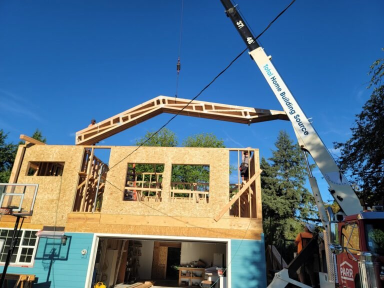 Crane lifting a roof truss above framed walls
